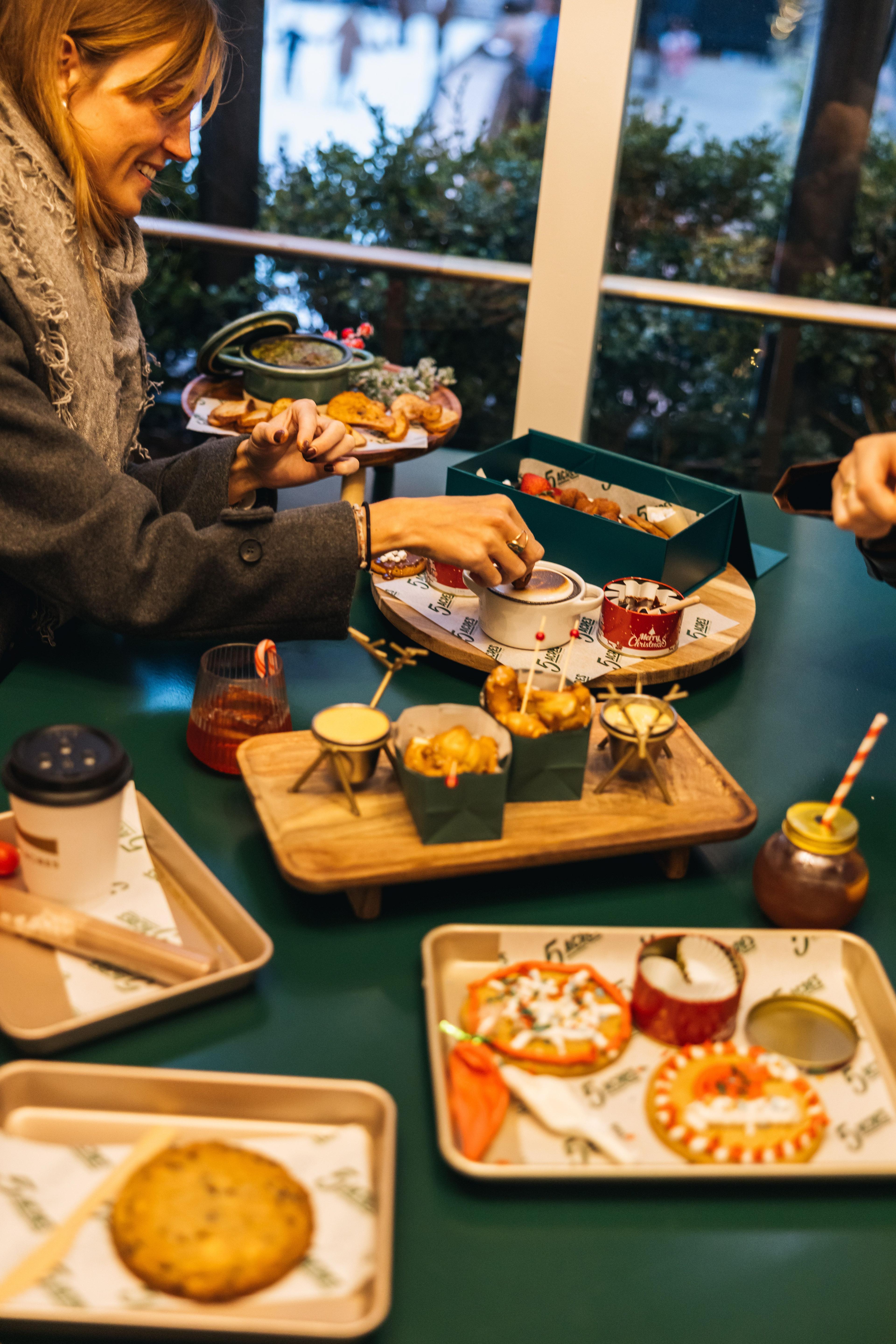 a woman sharing drinks and light bites inside Rockefeller Center's Après Skate Chalets