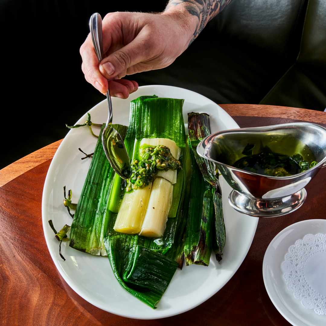 A hand pouring sauce on a plate of vegetables from Le Rock at Rockefeller Center