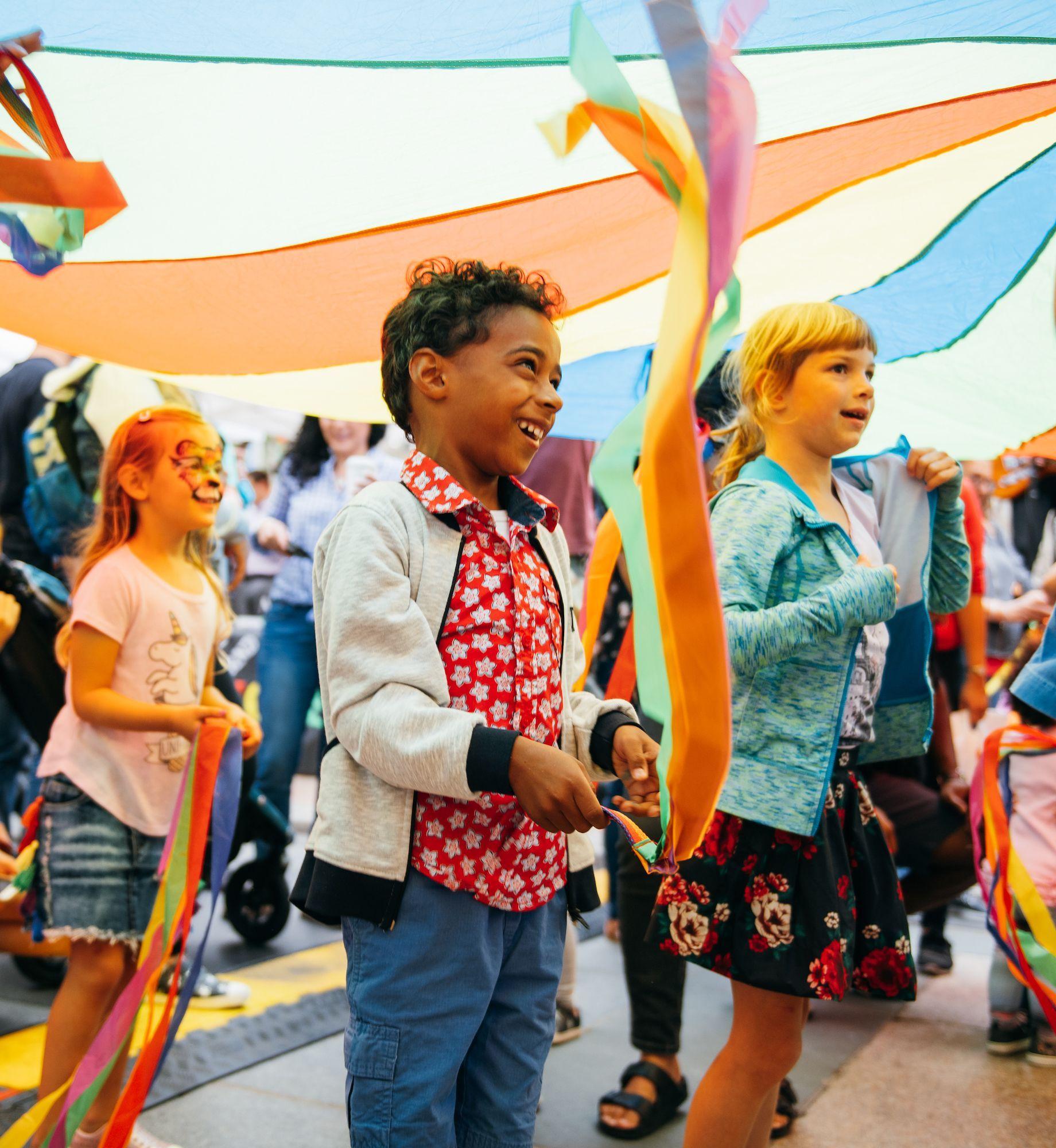 Three kids standing under a multicolored tent