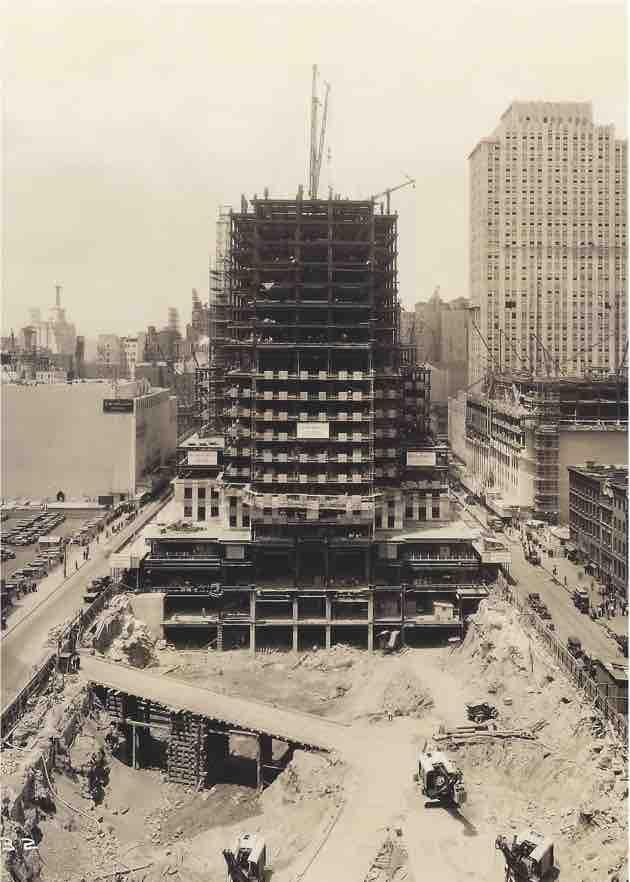 Black-and-white photo of Rockefeller Center under construction in 1931, showing a steel framework rising above an active worksite.
