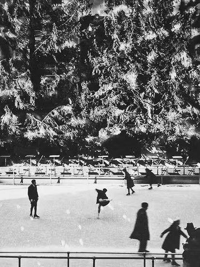 Black-and-white photo of skaters on the Rockefeller Center rink in 1936, with two Christmas trees towering above the ice.