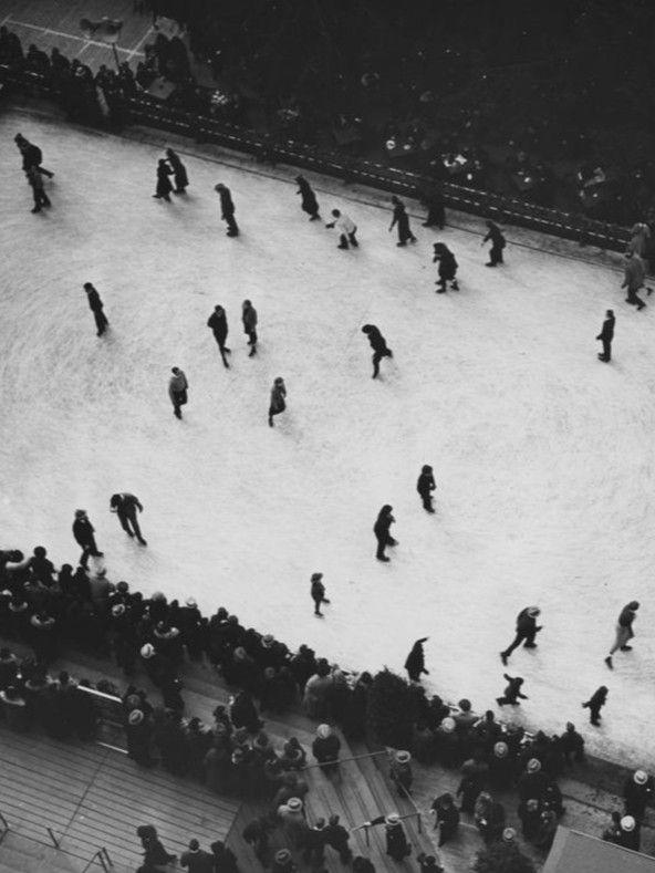 Overhead black-and-white photo of a crowded Rockefeller Center skating rink on New Year’s Day 1956, surrounded by spectators.