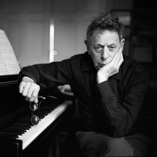 Philip Glass sitting next to a piano