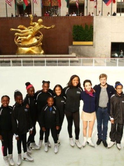 Color photo of a group of young skaters posing with Olympic ice dancers Meryl Davis and Charlie White on the Rockefeller Center rink.