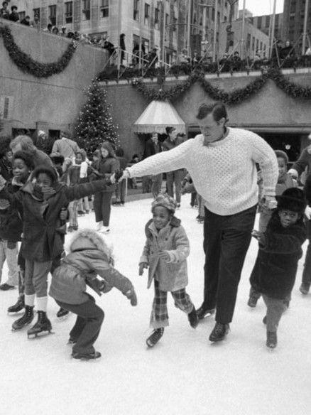 Black-and-white photo of Robert F. Kennedy skating with a group of children at Rockefeller Center during a holiday skating party in the 1960s.