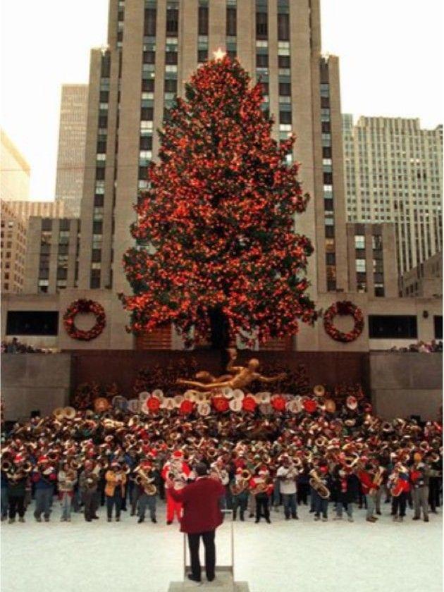 Color photo of a large group of tuba players performing in front of the Rockefeller Center Christmas Tree in 1997.