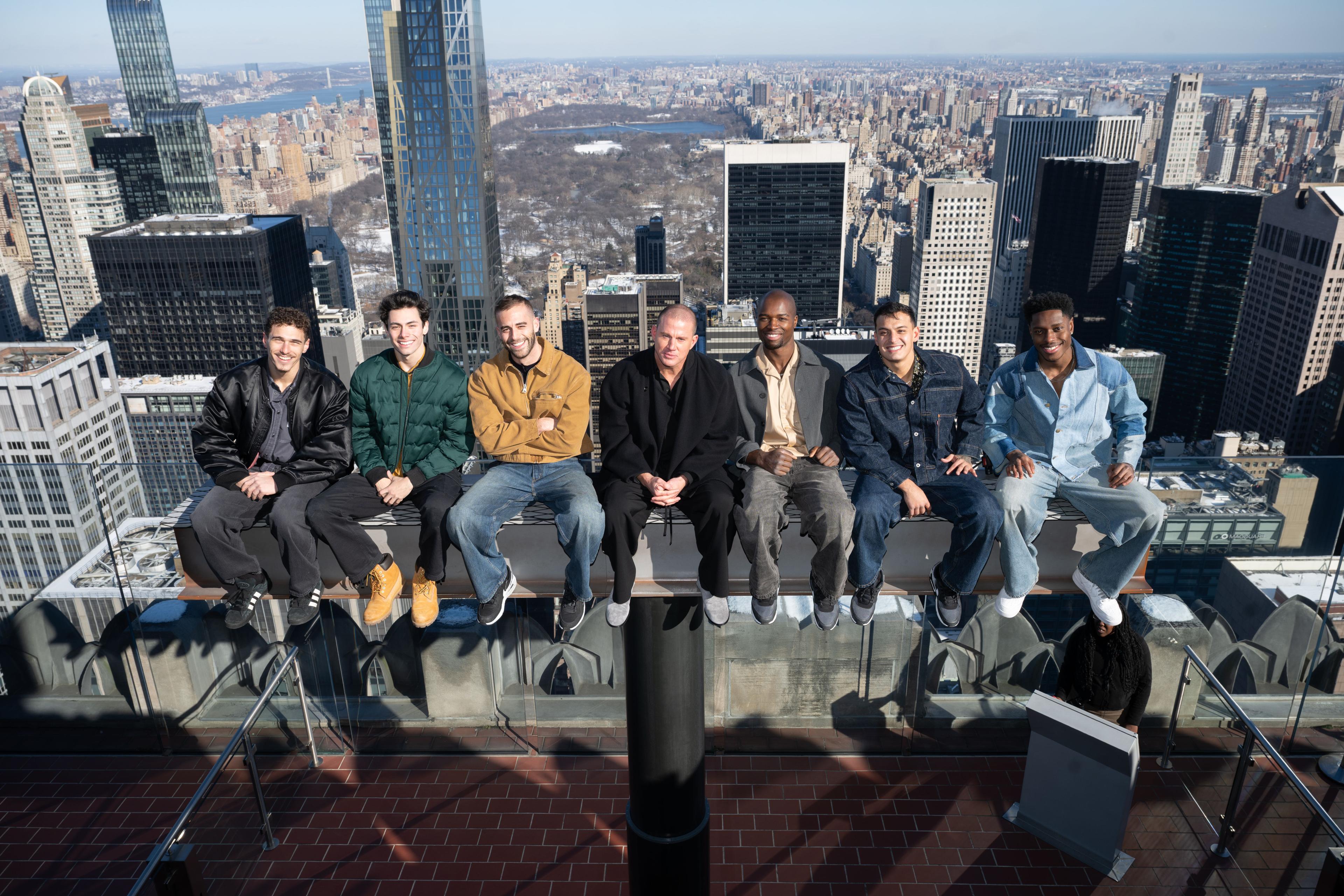 A group of smiling men on the beam at top of the rock