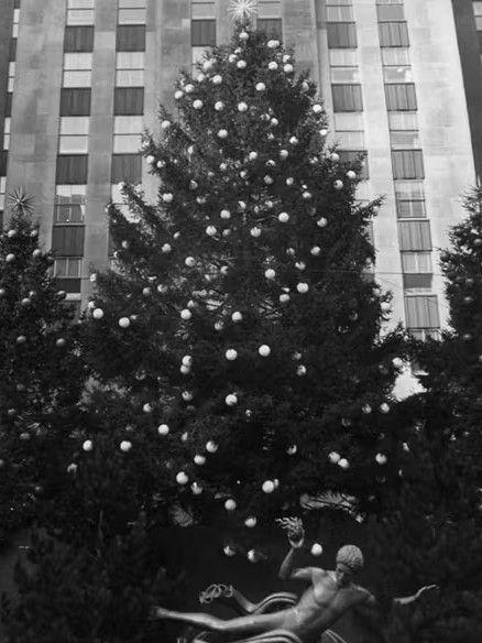 Black-and-white photo of multiple Christmas trees at Rockefeller Center in 1942, decorated simply during World War II with minimal lighting.