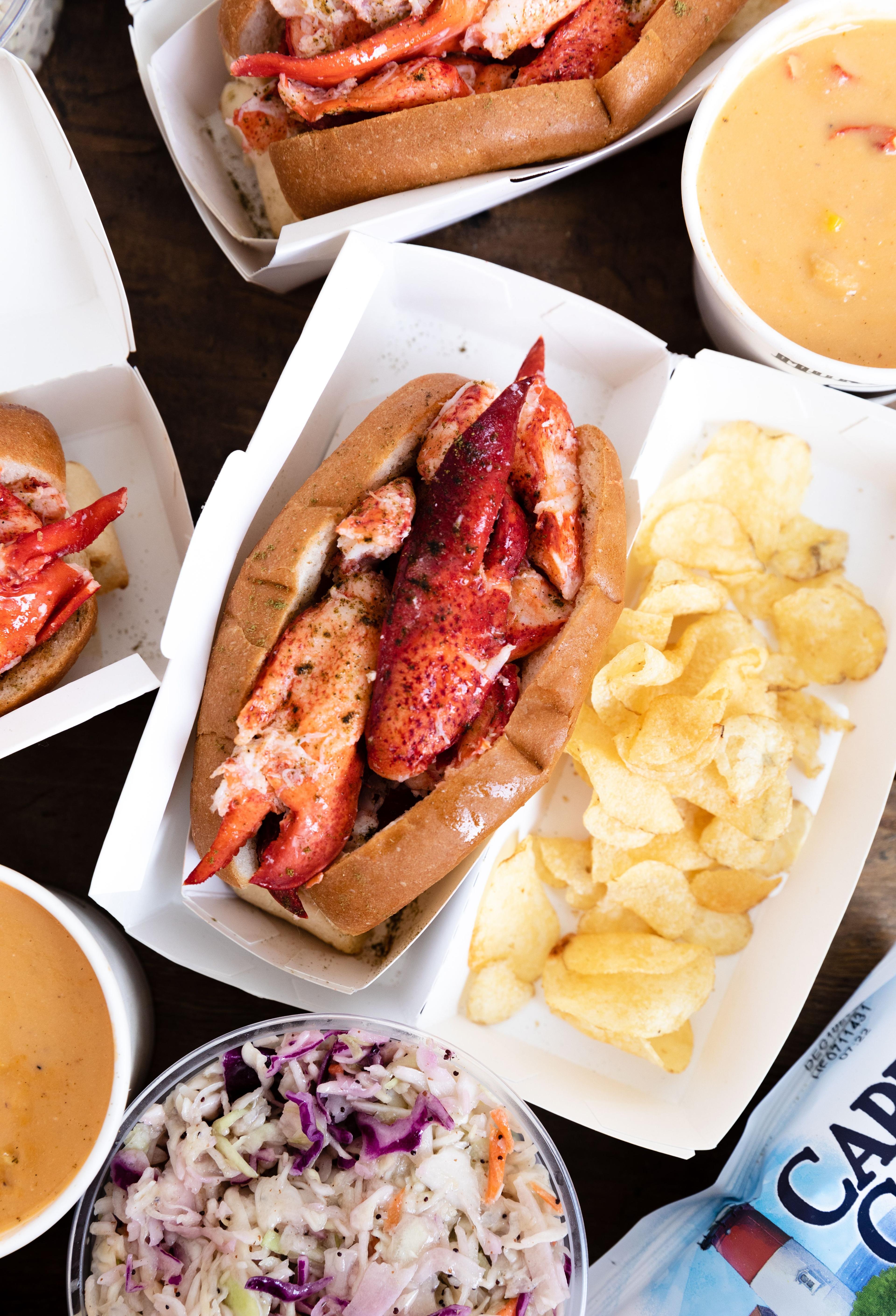 lobster roll, chips, and sides on a table