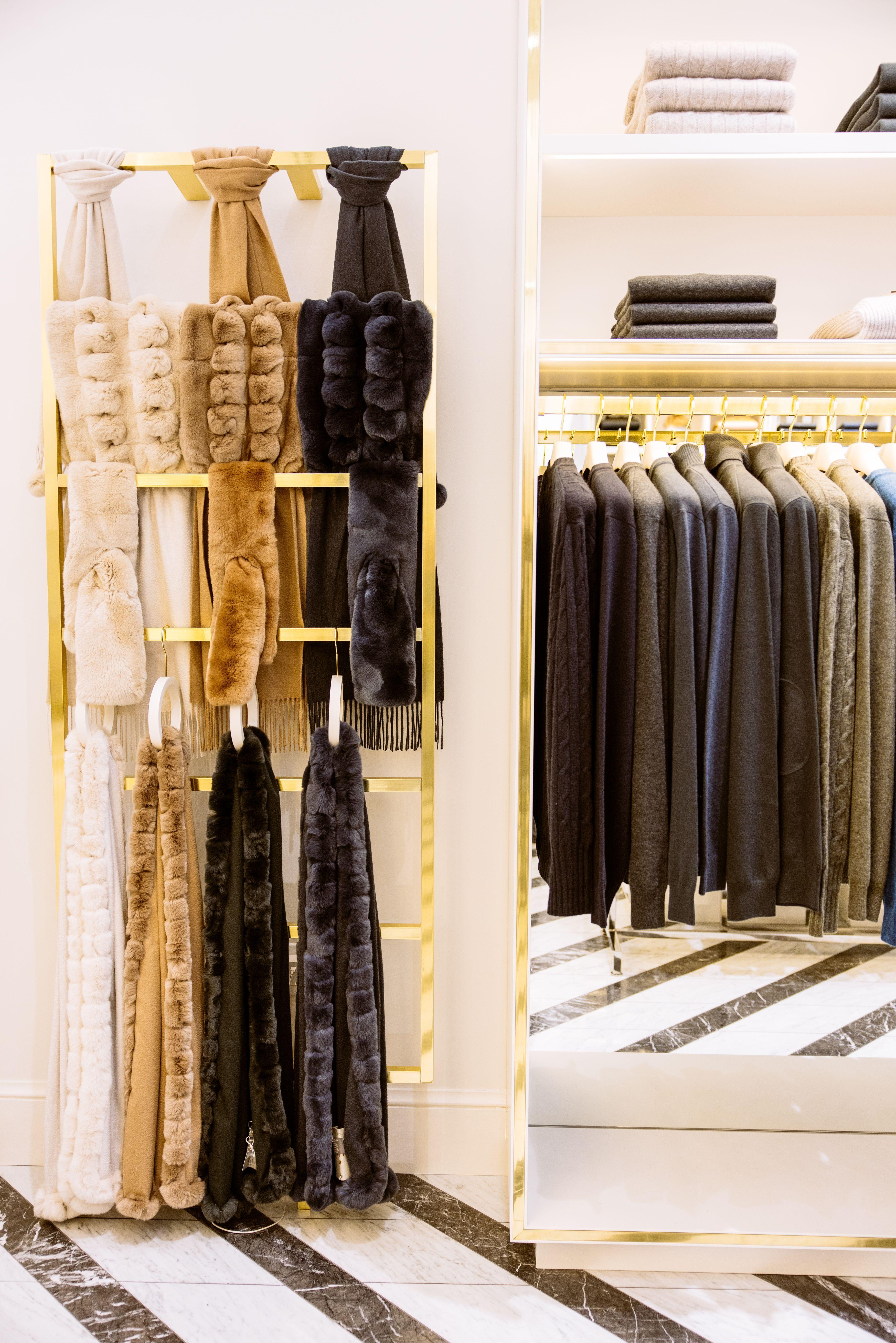Fur scarves hanging on a display next to a clothes rack of sweaters