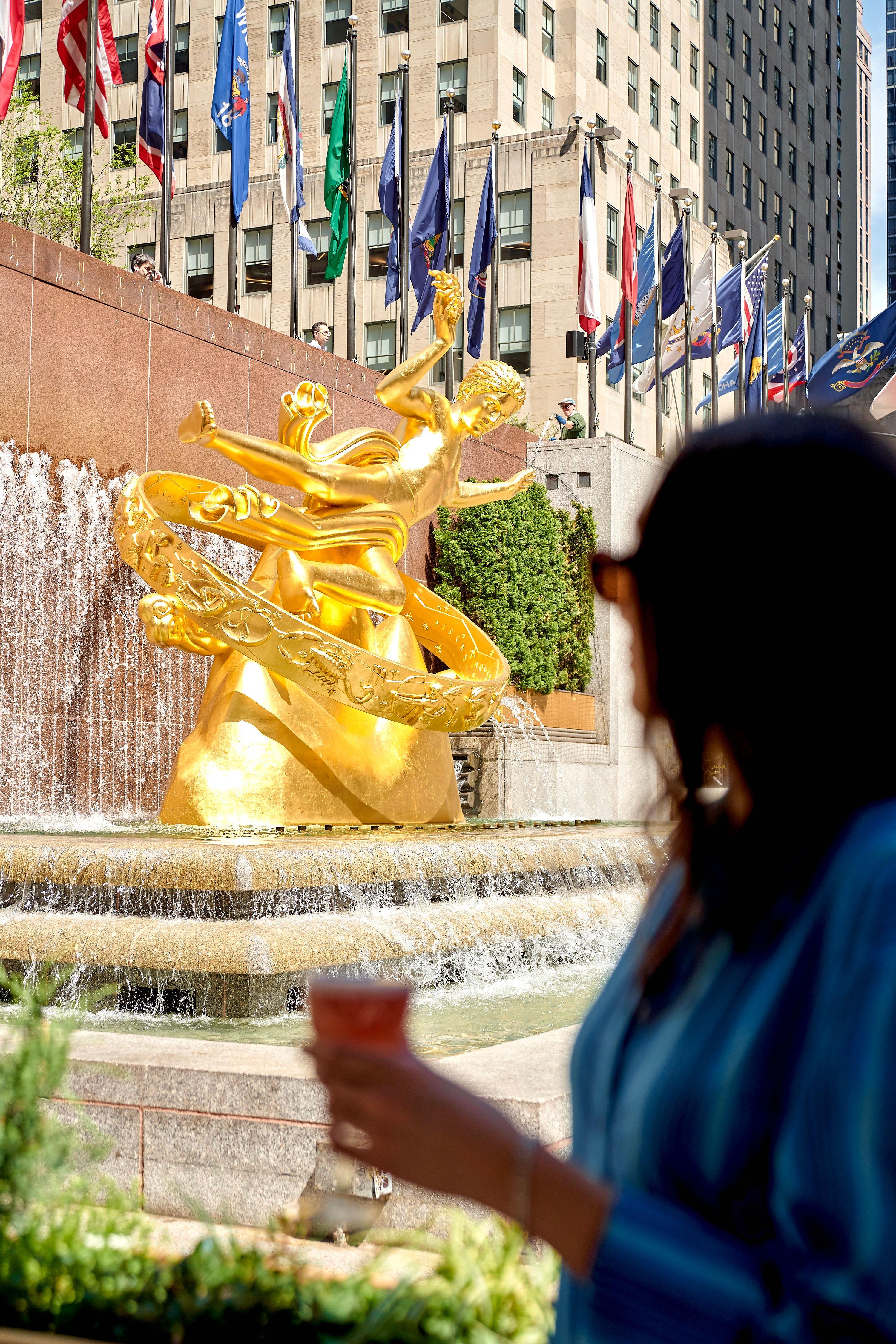 woman with a drink with gold prometheus statue in the background