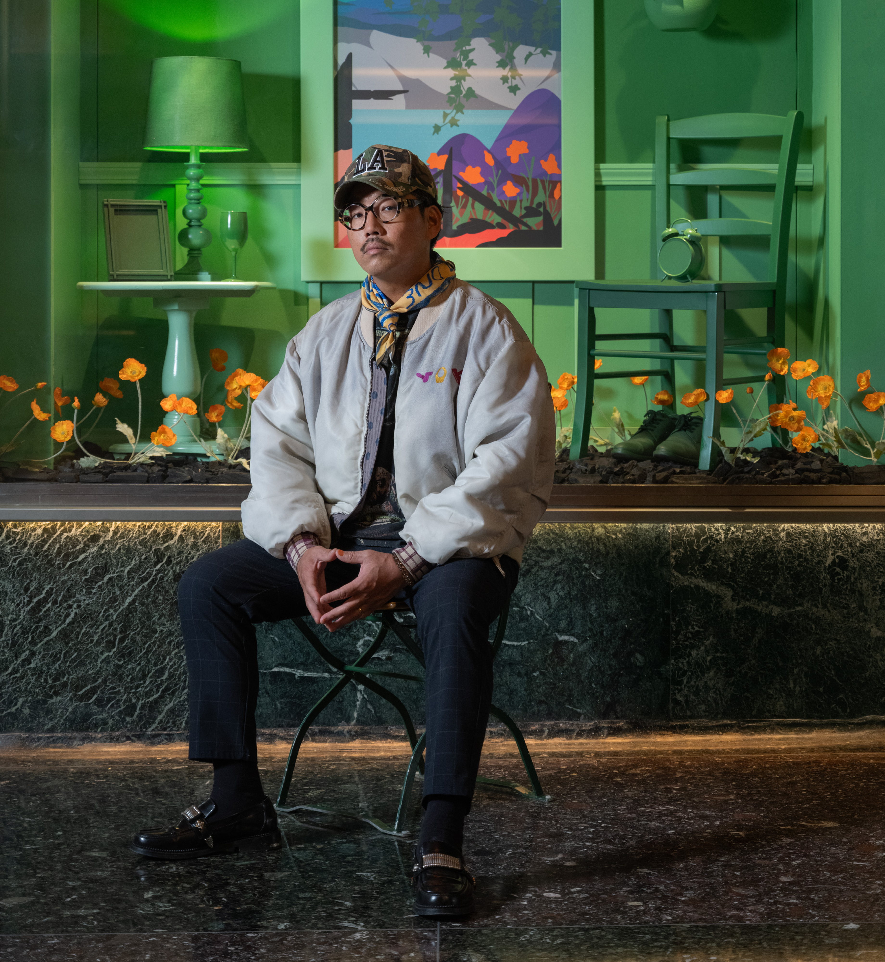 Artist Greg Ito sits in front of artwork from his Art in Focus exhibit, now on display at Rockefeller Center